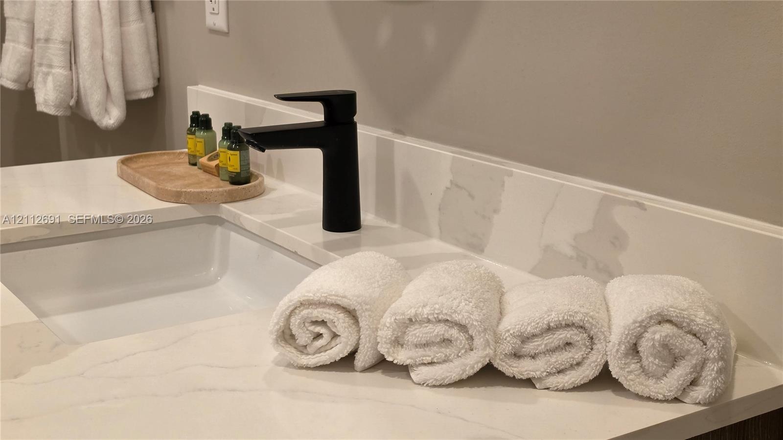 Bathroom vanity featuring a light-toned countertop with integrated backsplash, rectangular undermount sink, and matte black single-handle faucet