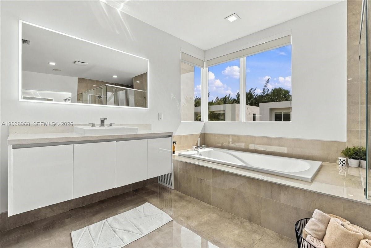 Modern bathroom featuring a wall-mounted floating vanity with a rectangular sink, expansive LED-backlit mirror, large-format tile flooring, built-in s
