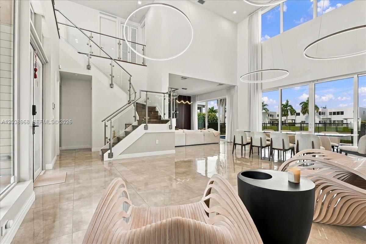 Double-height ceiling, floor-to-ceiling windows, polished tile flooring, glass-panel staircase railing, and modern circular pendant lighting