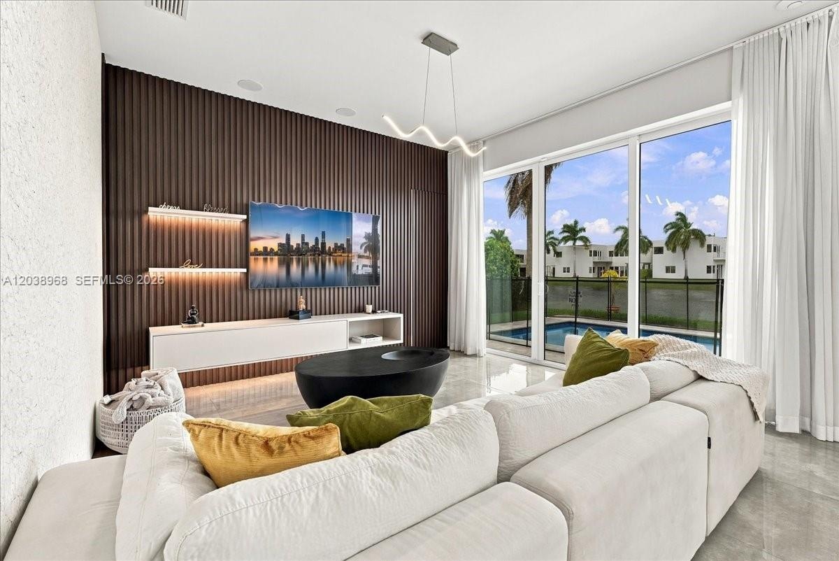 Living area featuring an accent wall with vertical fluted paneling, integrated floating cabinetry, custom illuminated shelving, a sculptural light fix