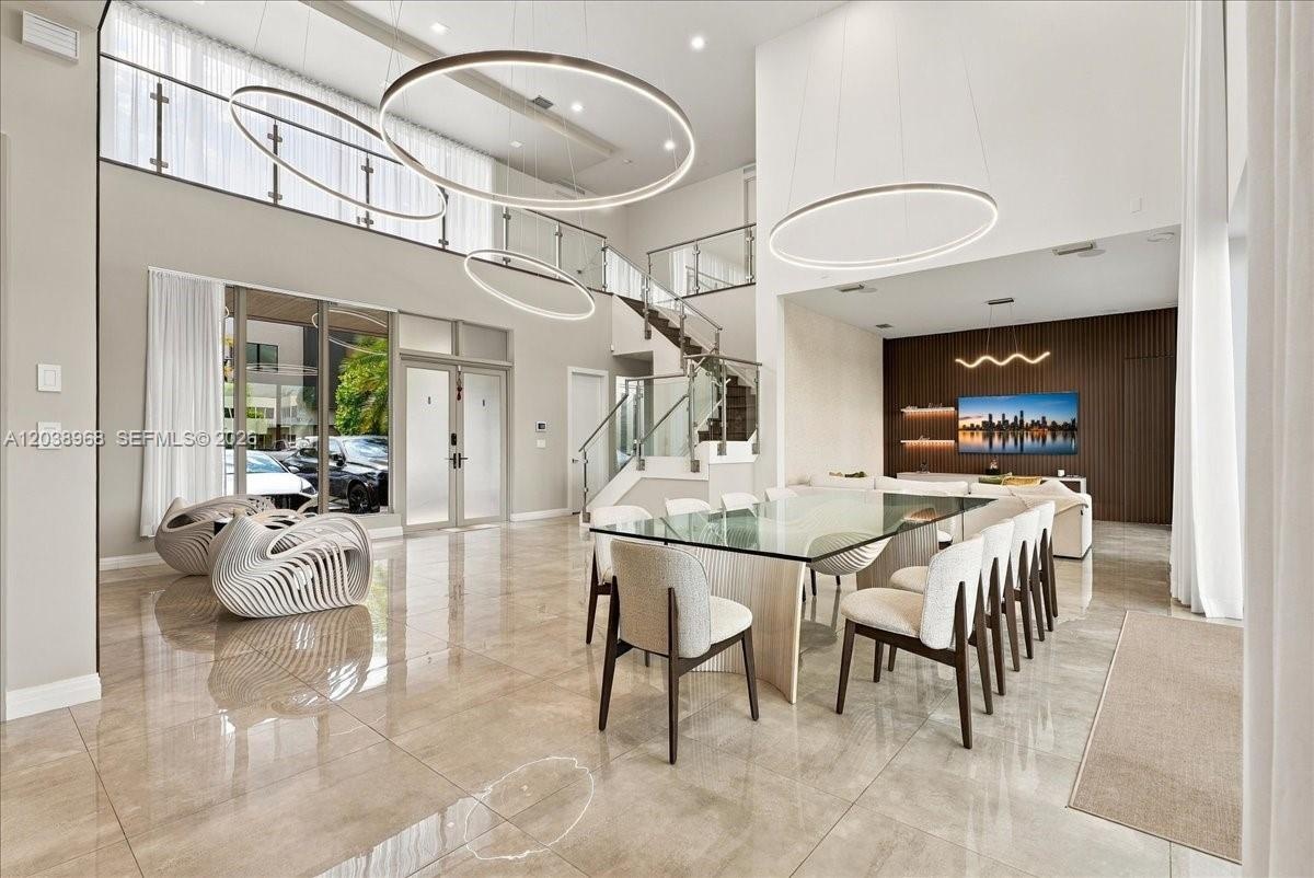 Double-height ceiling with large-scale circular pendant lighting, polished stone-finish flooring, glass-railed staircase, and decorative vertical wood