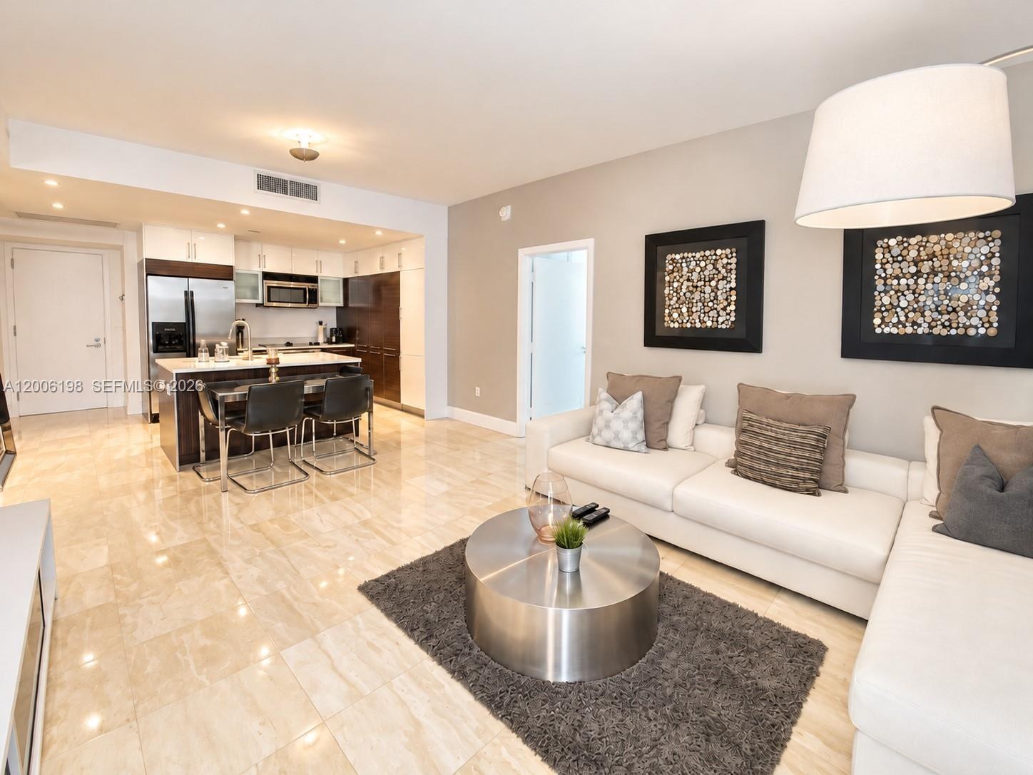 Open-concept interior featuring light-toned stone tile flooring, cabinetry with contrasting white and dark wood-finish surfaces, stainless steel kitch