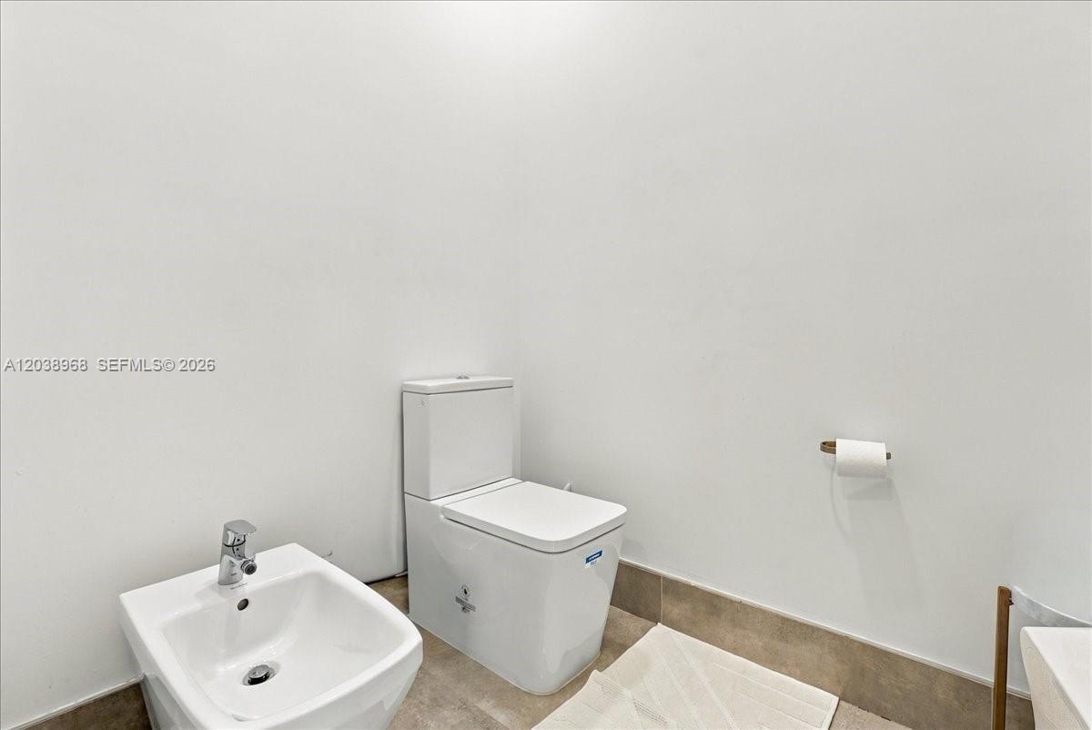 White porcelain toilet and matching bidet featuring chrome hardware, complemented by neutral tile flooring