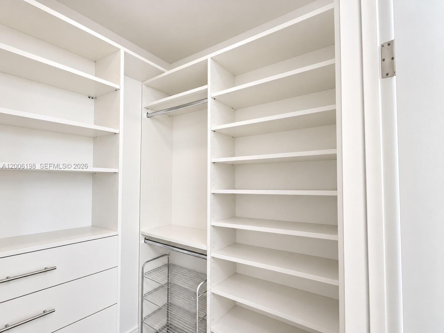 Custom white built-in storage system featuring floor-to-ceiling shelving, hanging rods, integrated drawers with horizontal pulls, and a metal wire rac