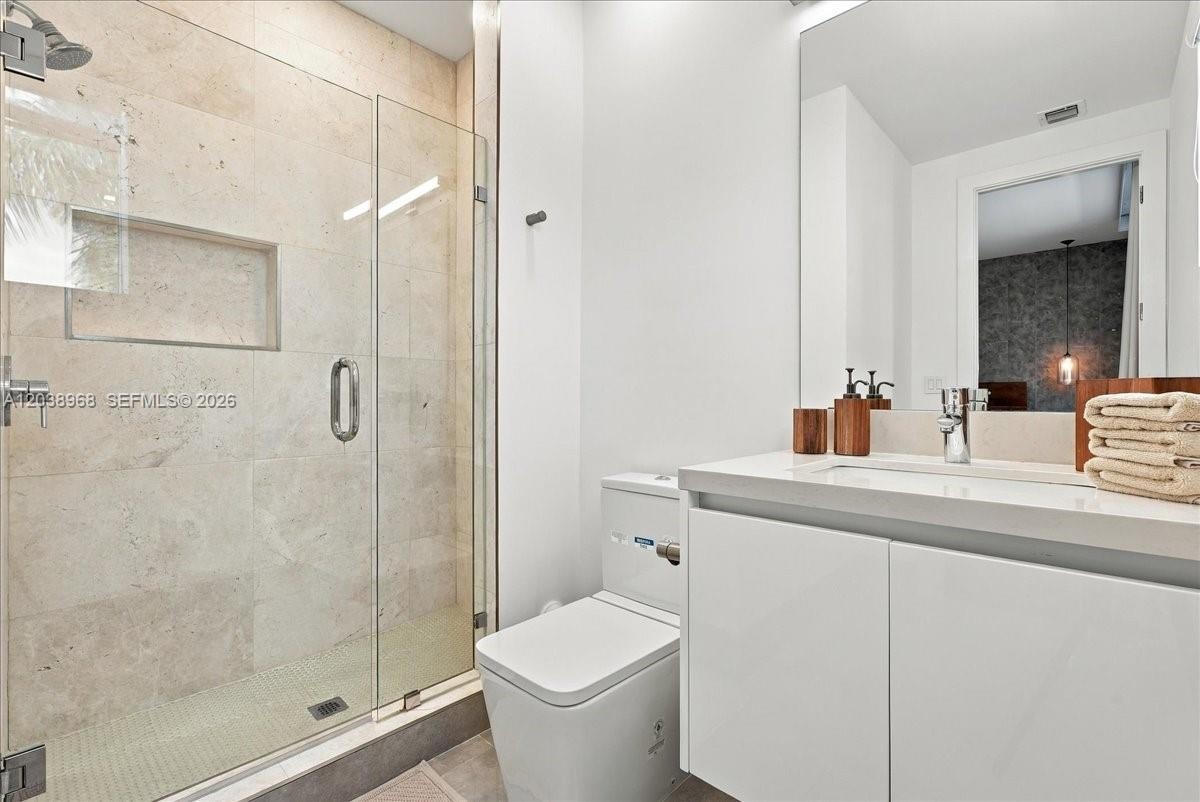 Bathroom featuring a walk-in shower with stone tile surround, integrated shower niche, glass enclosure, floating vanity with an integrated basin, and 