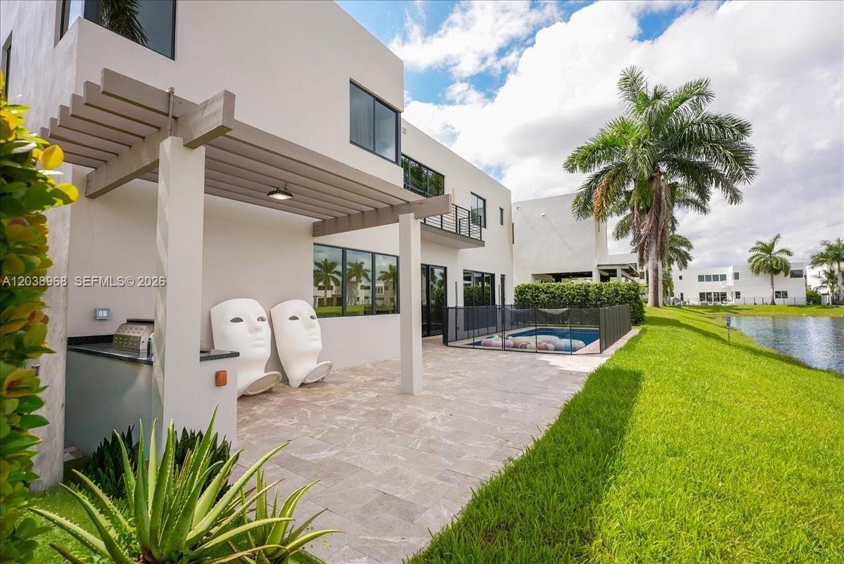 Stucco exterior featuring a covered pergola, stone-paved patio, built-in outdoor kitchen, and a pool with perimeter fencing
