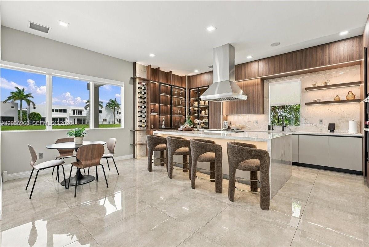 Contemporary kitchen featuring a spacious stone-topped island, floor-to-ceiling cabinetry, built-in wine storage, stainless steel range hood, and larg