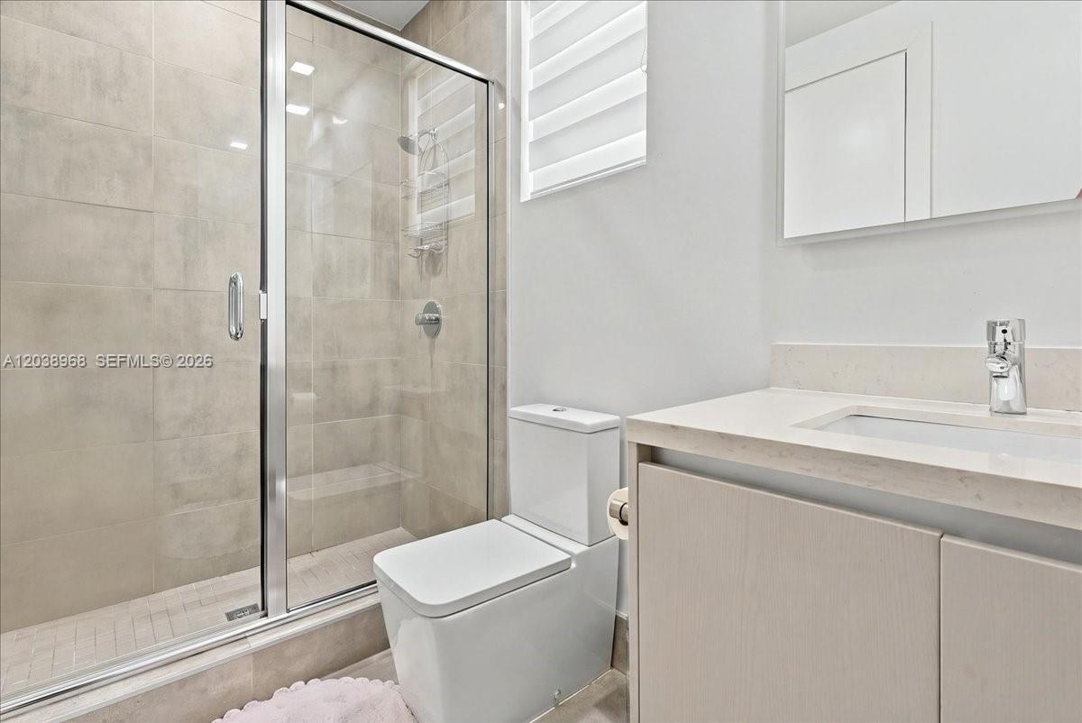 Glass-enclosed shower with large-format wall tile, light wood-finish vanity, light-toned countertop with integrated sink, and polished chrome fixtures
