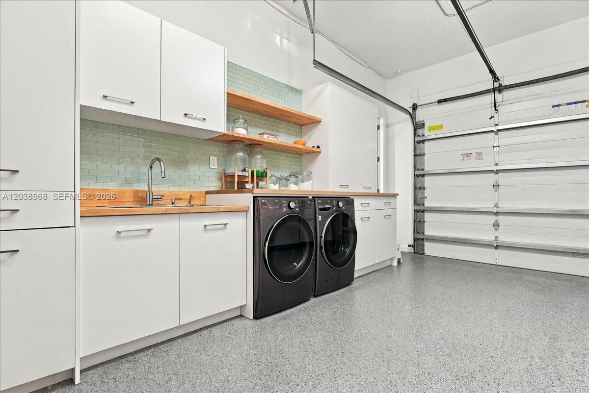 Garage utility area featuring white cabinetry, wood-finish countertops, a stainless steel sink with a chrome faucet, light green subway tile backsplas