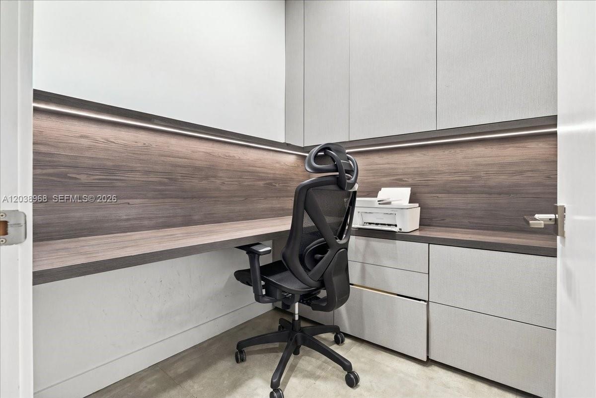 Built-in L-shaped wood-finish desk with integrated under-cabinet LED lighting, matte grey cabinetry, floor-to-ceiling storage, and solid-surface count