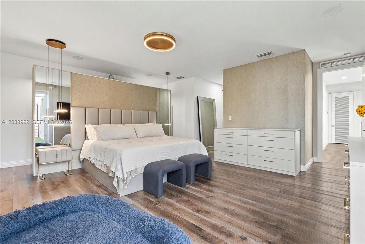 Wood-finish flooring, custom built-in headboard wall with integrated mirrored panels, modern circular flush-mount lighting, and contemporary pendant f