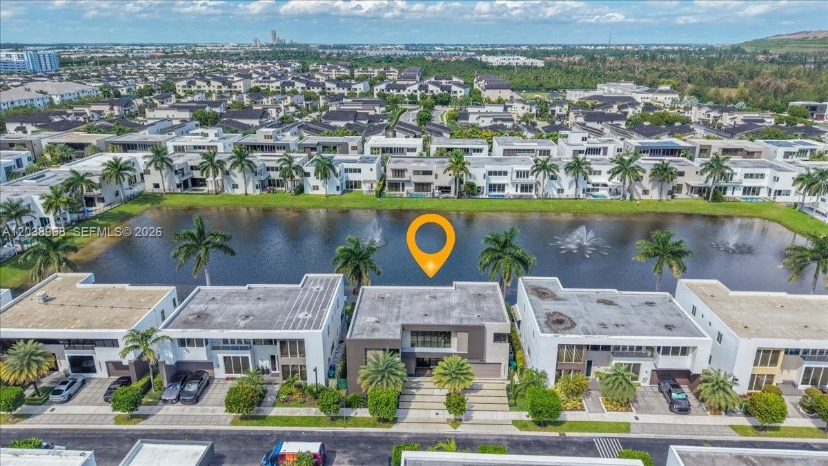 Aerial perspective of a multi-story residence featuring a flat roofline, integrated two-car garage, paved driveway, and direct water frontage on a com