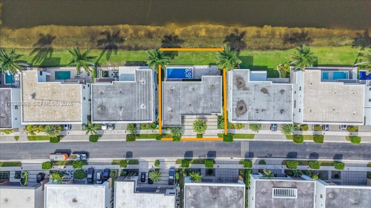 Aerial perspective of waterfront property featuring a private swimming pool, concrete paver patio, and mature landscaping