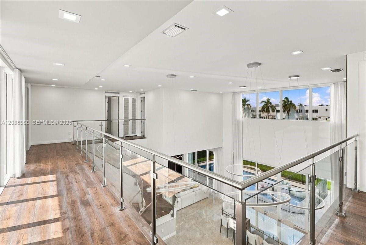 Open-concept landing featuring wood-finish flooring, glass-panel railing with metal hardware, recessed lighting, and double-height windows