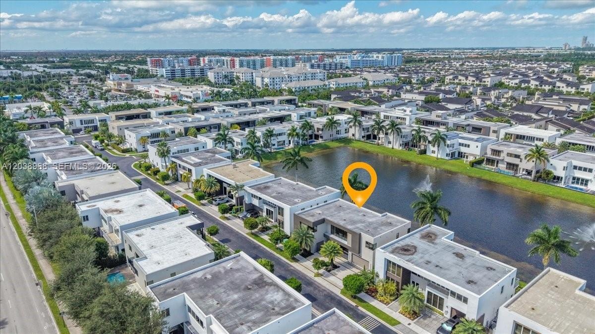 Aerial perspective of a two-story residence featuring a flat roofline, attached multi-car garage, water frontage, and mature palm landscaping