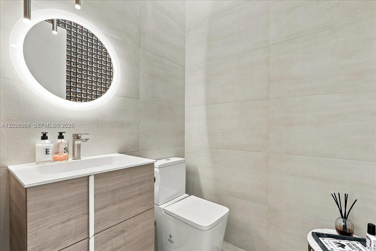 Modern vanity with a wood-finish cabinet and integrated sink, illuminated oval wall mirror, and large-format tile wall cladding