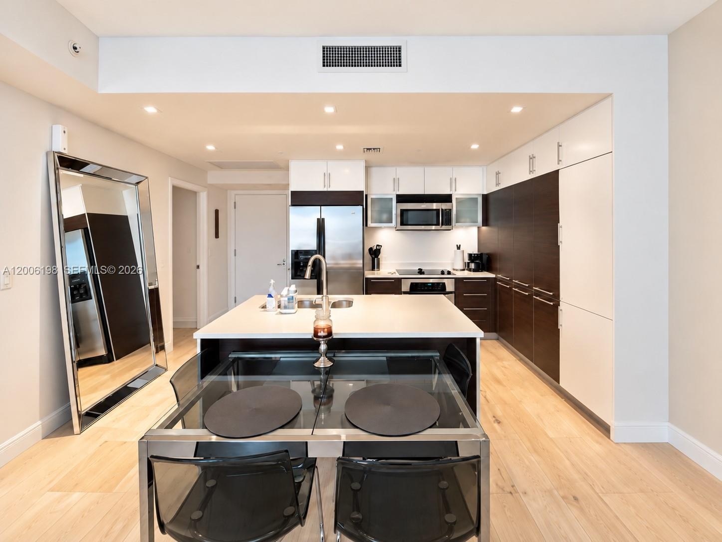 Modern kitchen featuring two-tone flat-panel cabinetry, a central island with a solid-surface countertop, stainless steel appliances, and wood-finish 
