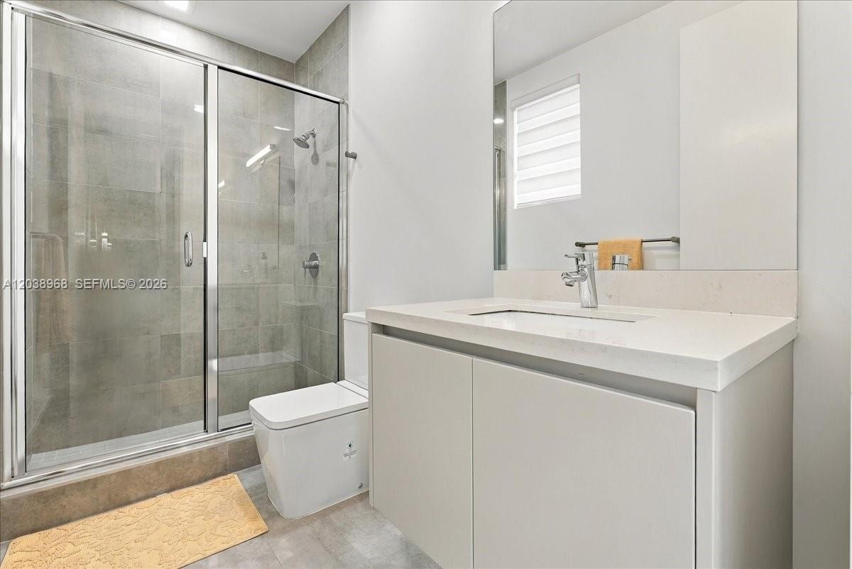 Modern bathroom featuring a floating vanity with a light-tone countertop, an integrated sink, a large wall-mounted mirror, and a walk-in shower with t