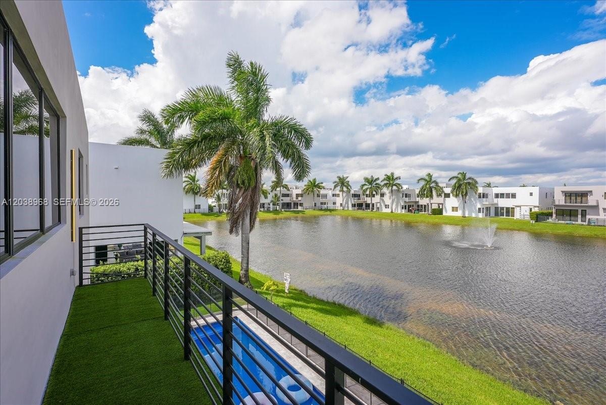 Balcony featuring synthetic turf flooring and black metal railing, overlooking a private pool and water feature