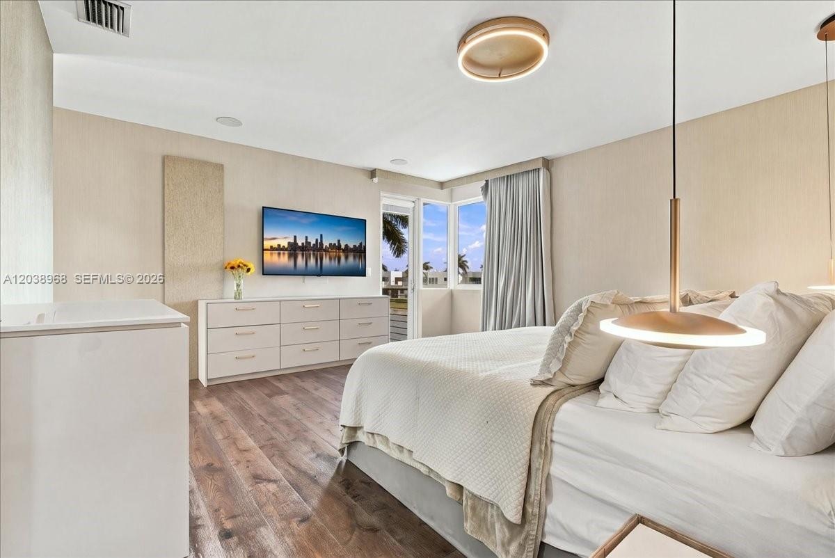 Room featuring wood-finish flooring, textured wall treatments, minimalist disc-style flush mount ceiling lighting, and suspended metallic pendant ligh
