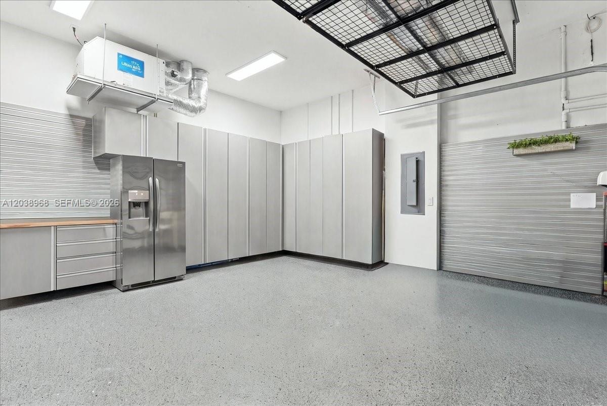 Garage interior featuring epoxy flooring, wall-to-wall built-in cabinetry, stainless steel refrigerator, overhead storage rack, and corrugated metal w
