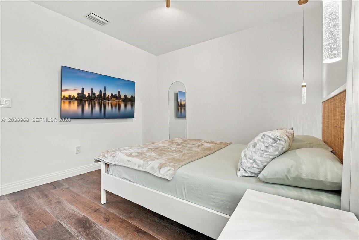 Wood-finish flooring, textured arched wall mirror, woven-texture headboard, and contemporary cylindrical pendant lighting