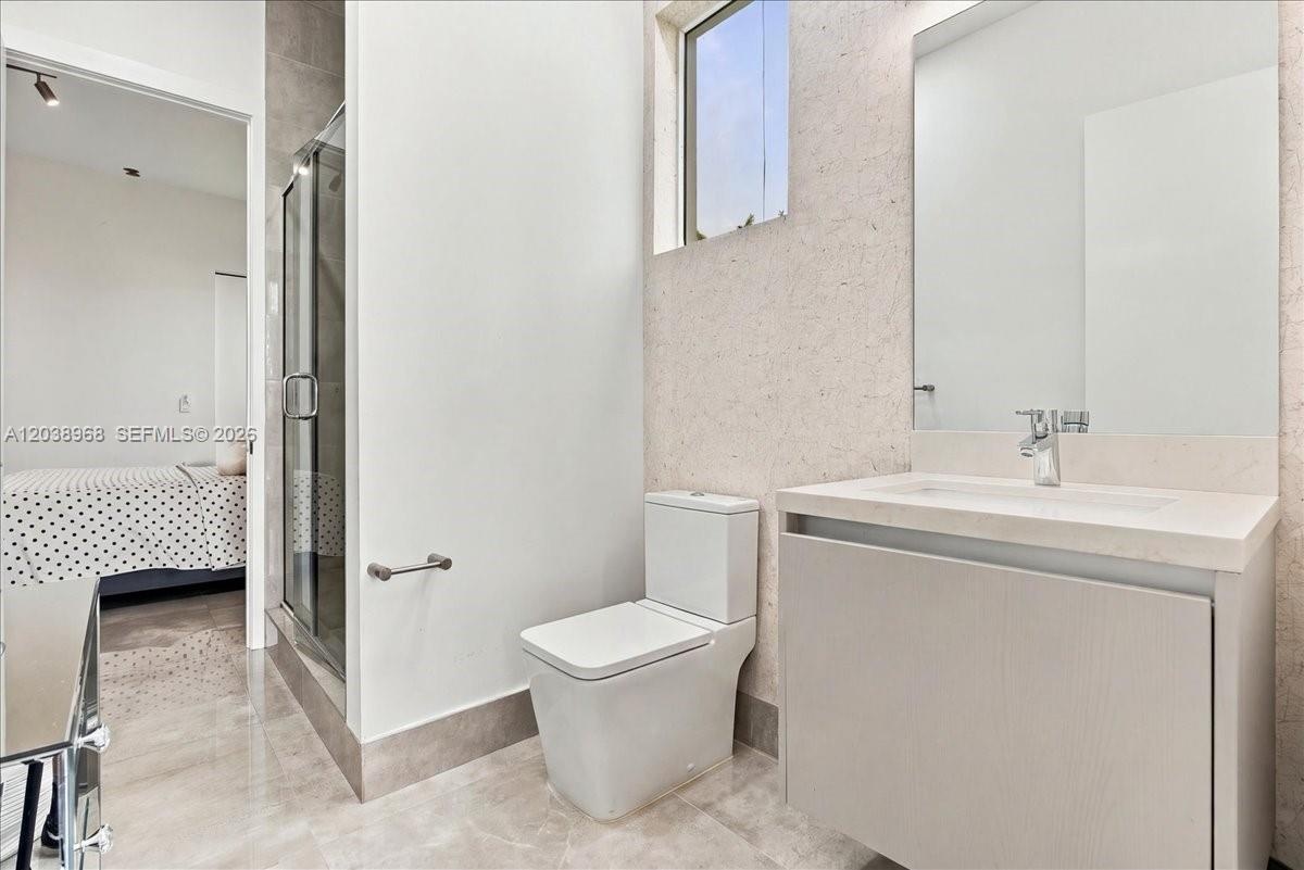 Floating vanity with stone countertop, integrated basin, glass-enclosed shower, stone-finish flooring, and recessed lighting
