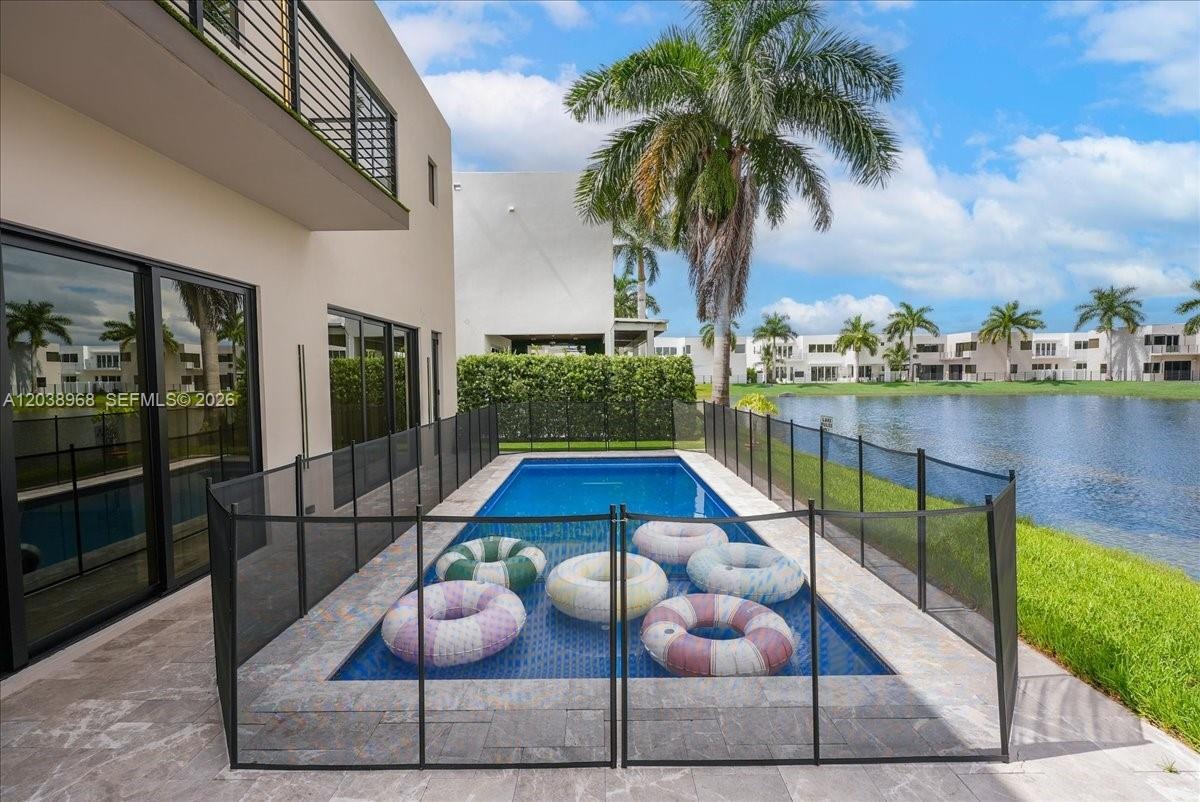 In-ground pool featuring stone paver decking, black mesh safety fencing, sliding glass doors, and waterfront positioning