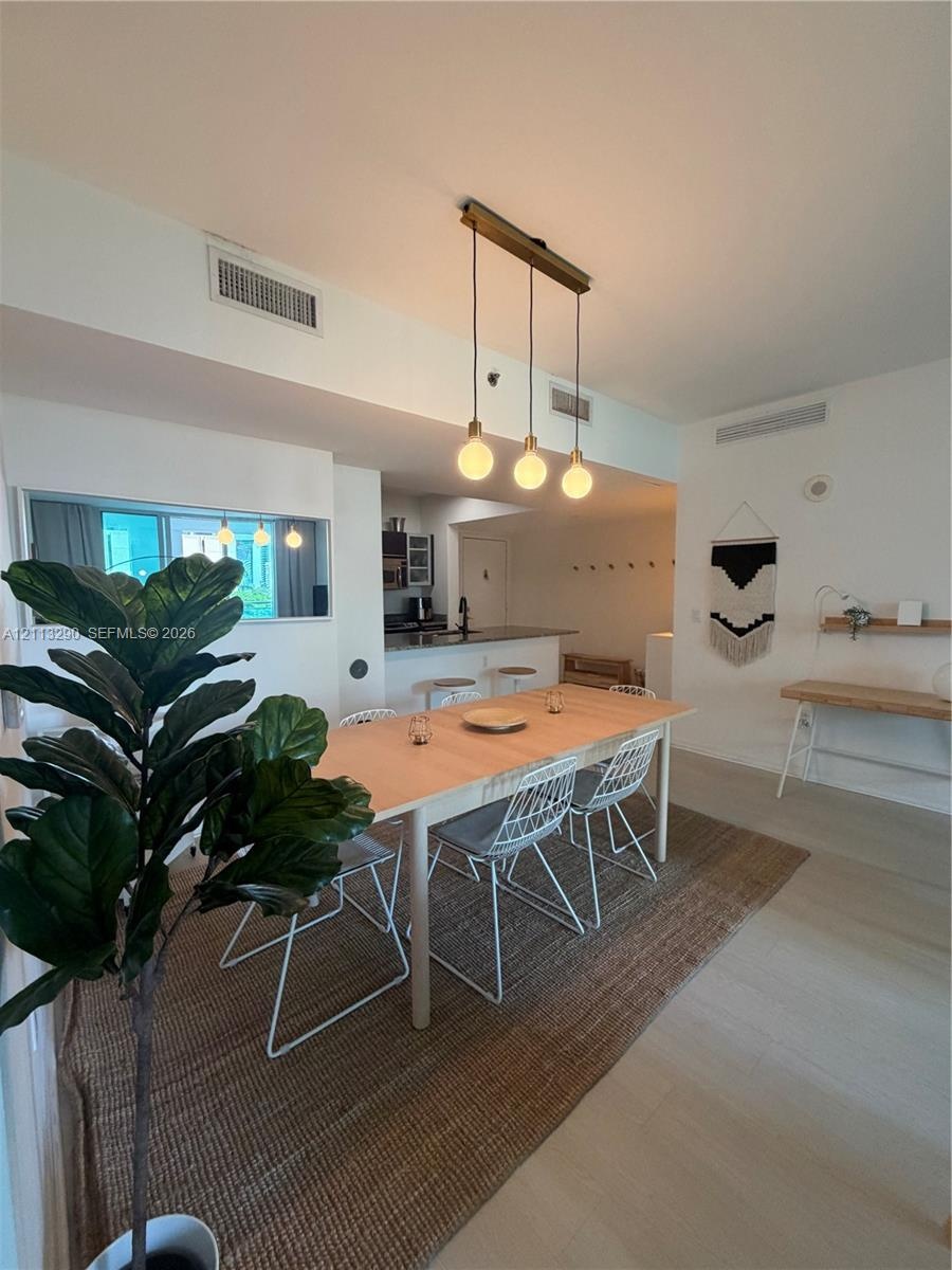 Open-concept interior featuring light-toned wood-finish flooring, a linear three-pendant light fixture, and a built-in wall shelf