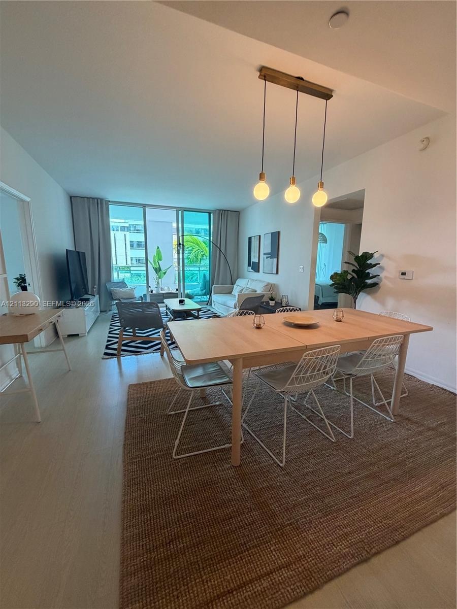 Open-concept living space featuring wood-finish flooring, floor-to-ceiling glass sliding doors, and a linear pendant light fixture with three exposed 