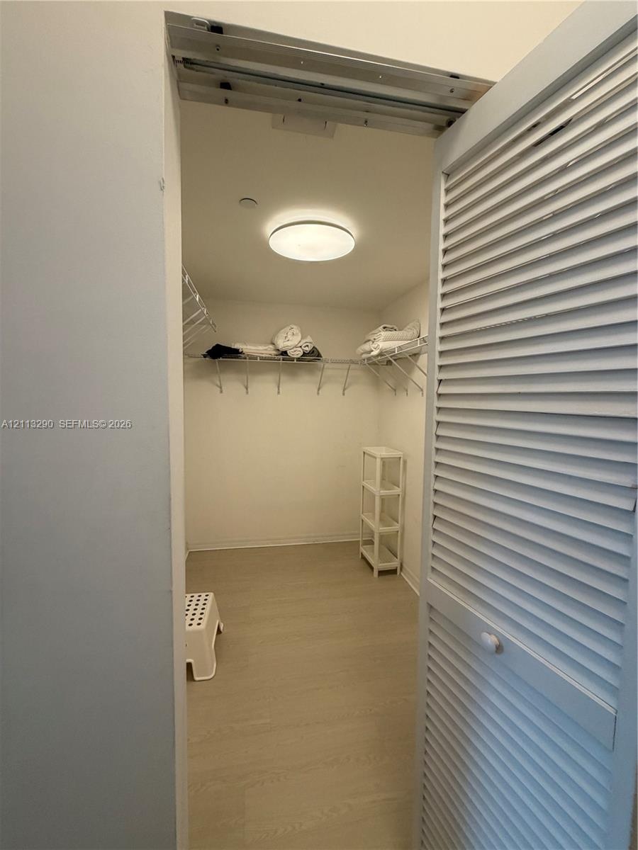 Storage closet featuring white louvered doors, neutral wood-finish flooring, and built-in wire shelving
