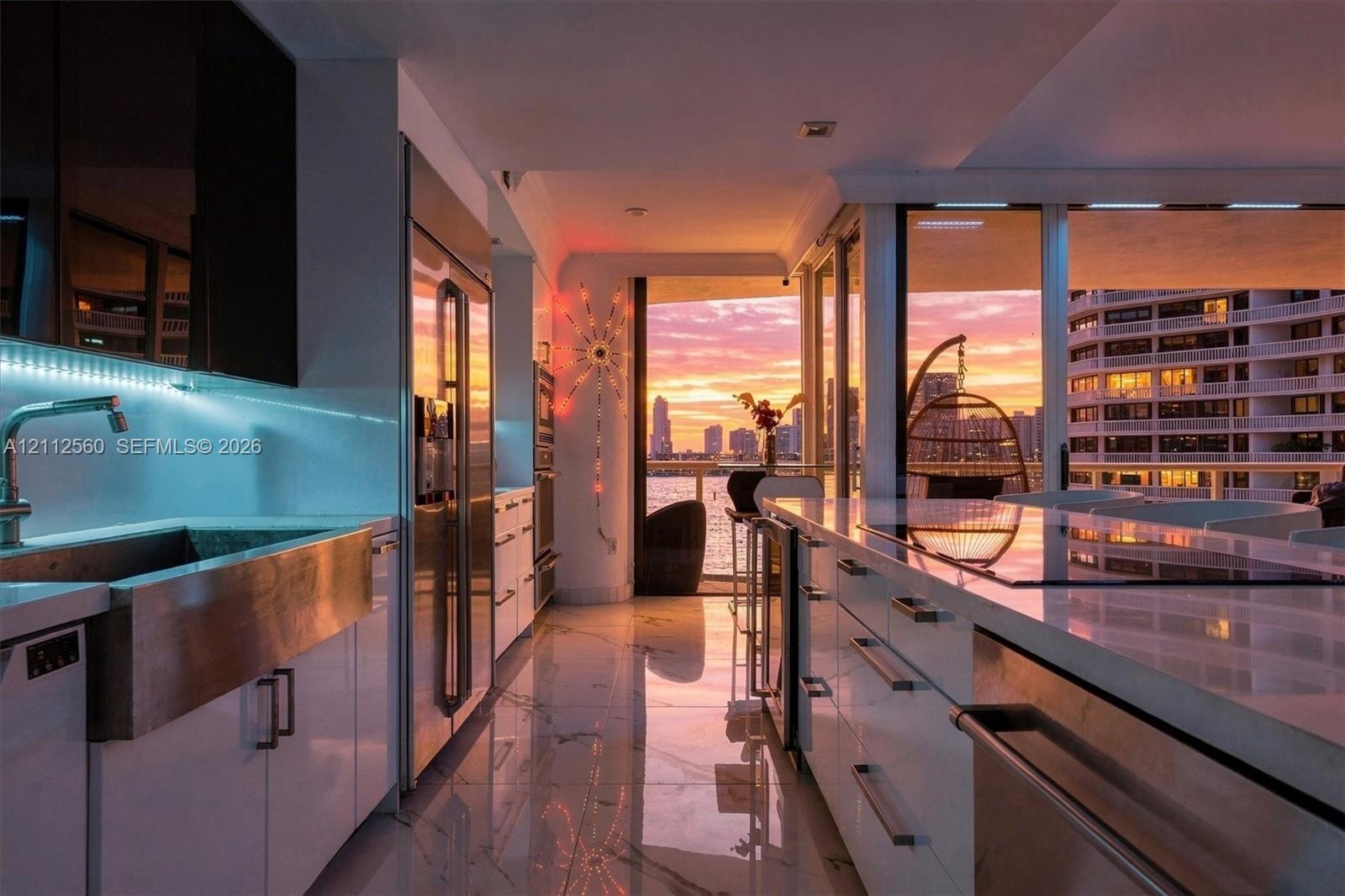 Modern kitchen featuring sleek white cabinetry, stainless steel apron-front sink, polished stone countertops, integrated stainless steel appliances, a
