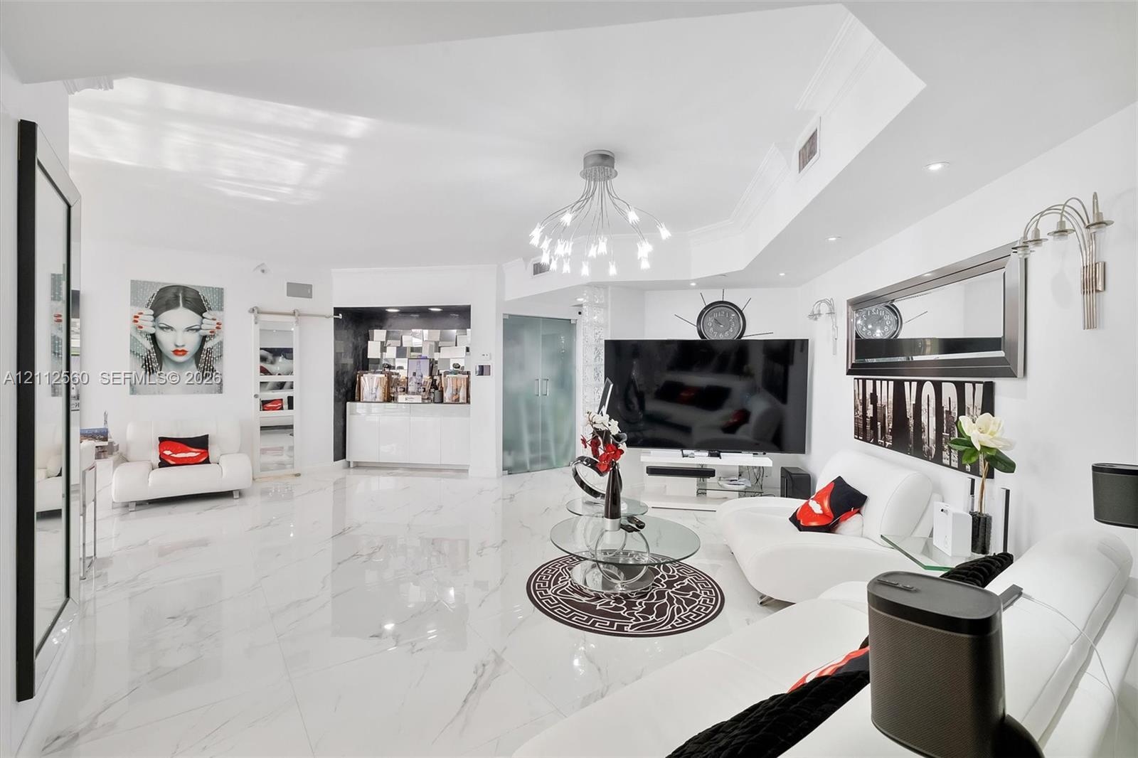 Large-format polished flooring, recessed ceiling lighting, multi-arm chandelier, built-in wet bar with high-gloss cabinetry, and frosted glass door