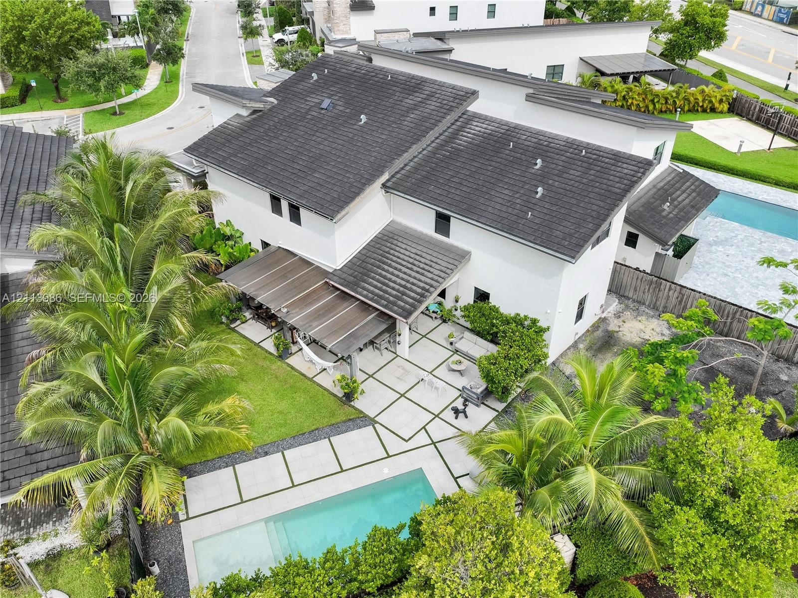 Modern two-story residence featuring a tile roof, an expansive paved patio, a rectangular swimming pool, and mature palm trees