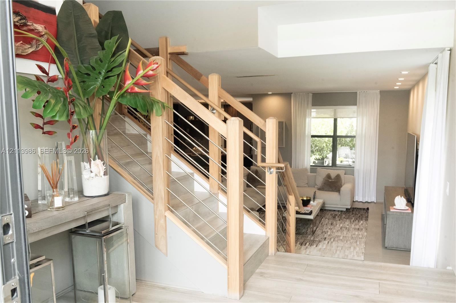 Staircase featuring light wood framing and horizontal steel tension cables, complemented by light wood-finish flooring and recessed ceiling lighting