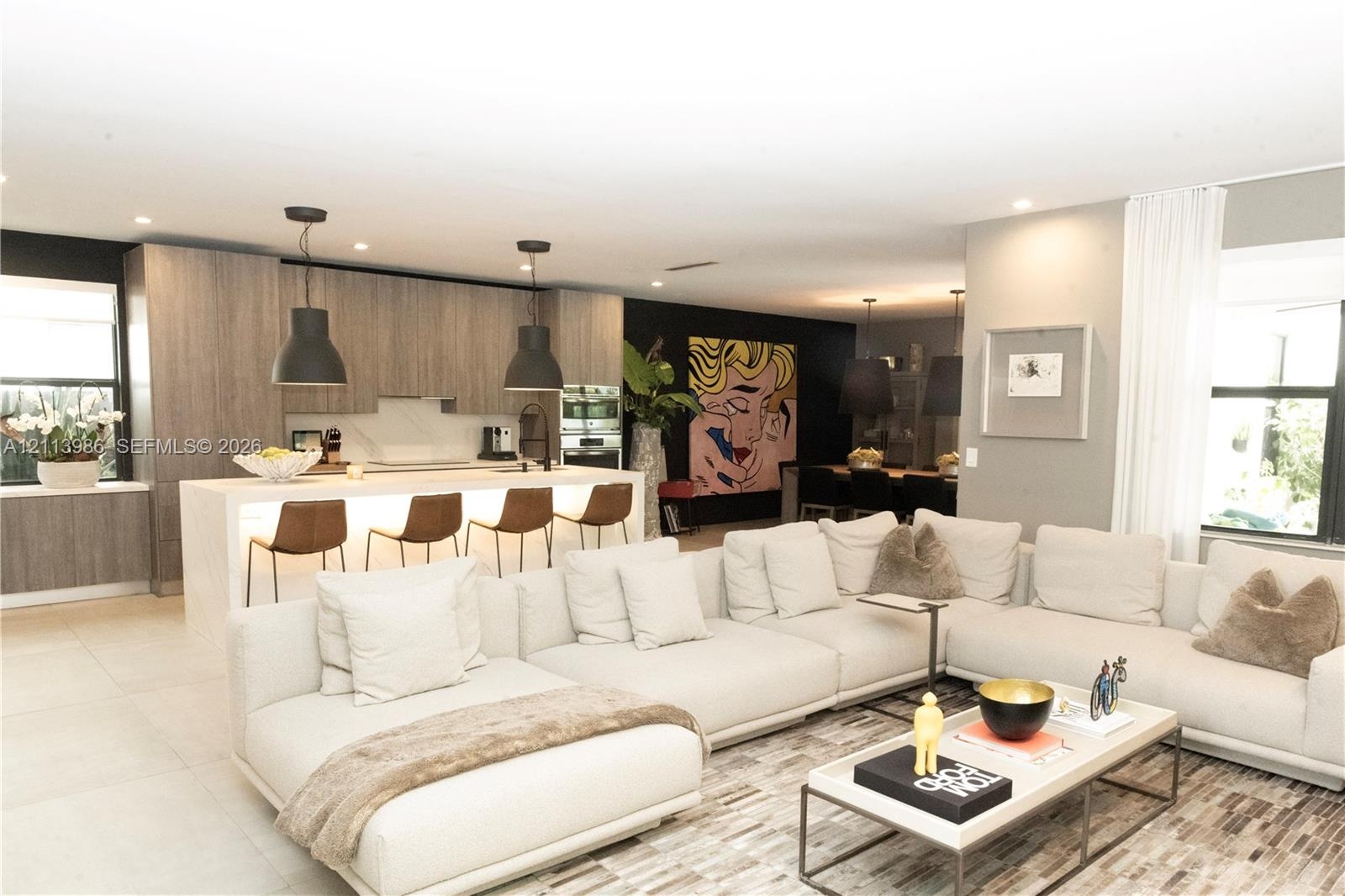 Open-concept interior featuring light wood-finish cabinetry, a large kitchen island with integrated under-counter lighting, stone slab surfacing, and 