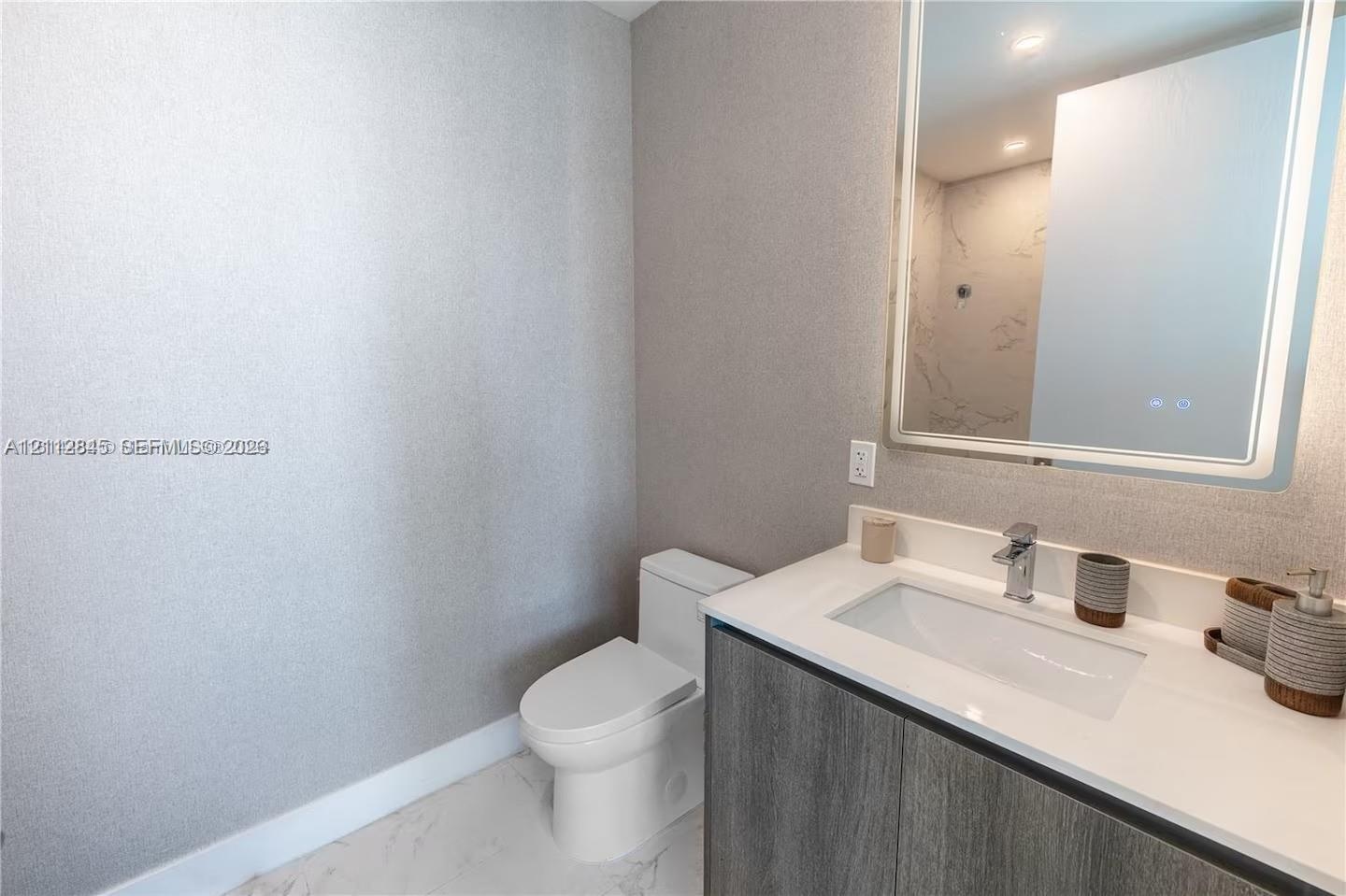 Modern vanity featuring a charcoal-finish cabinet, rectangular basin, and stone-surface countertop, complemented by a large integrated backlit mirror 