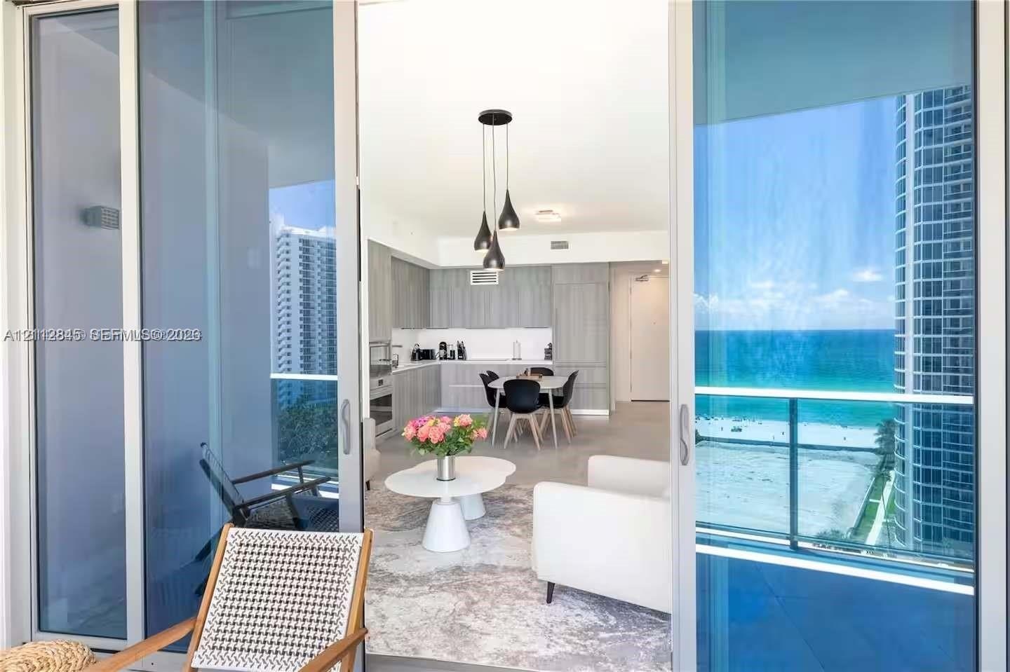 Full-height sliding glass doors opening to a covered balcony, integrated kitchen cabinetry, recessed ceiling lighting, pendant light fixture, and ocea