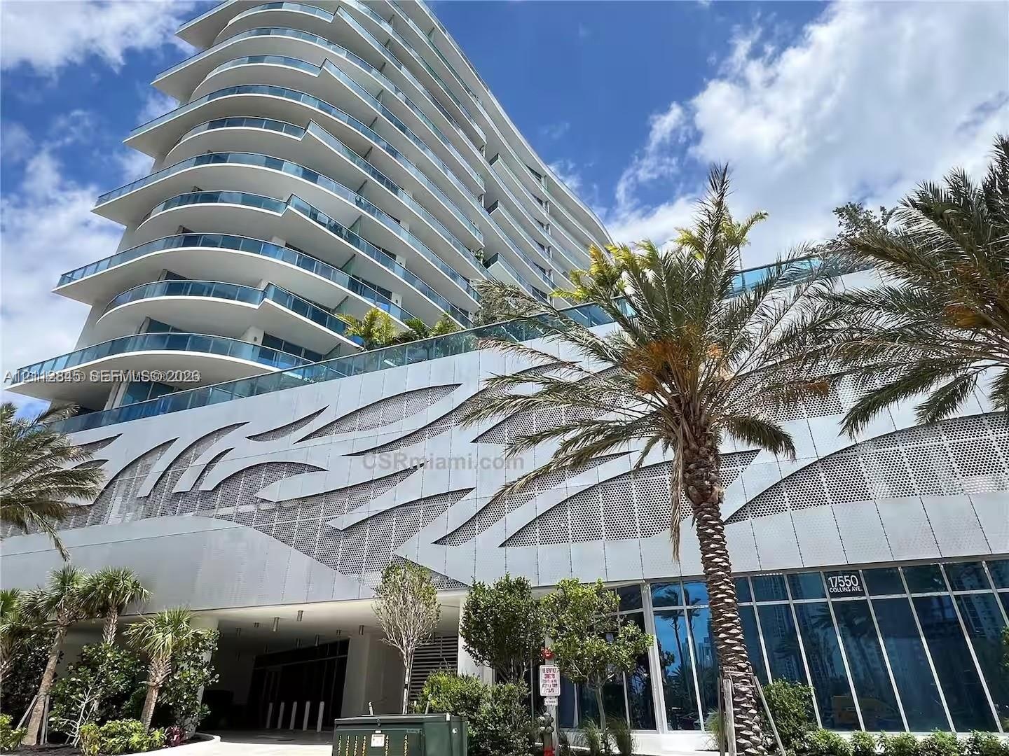 High-rise architectural exterior featuring tiered glass balconies, metallic geometric facade paneling, floor-to-ceiling glass windows, and mature palm