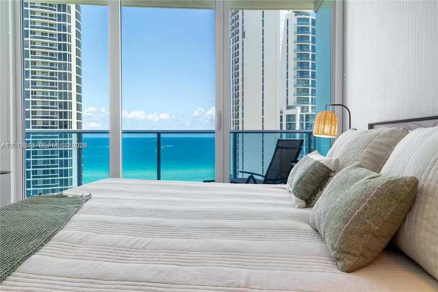 Floor-to-ceiling glass paneling featuring ocean and high-rise cityscape backdrops, with access to a private balcony enclosed by glass and metal railin