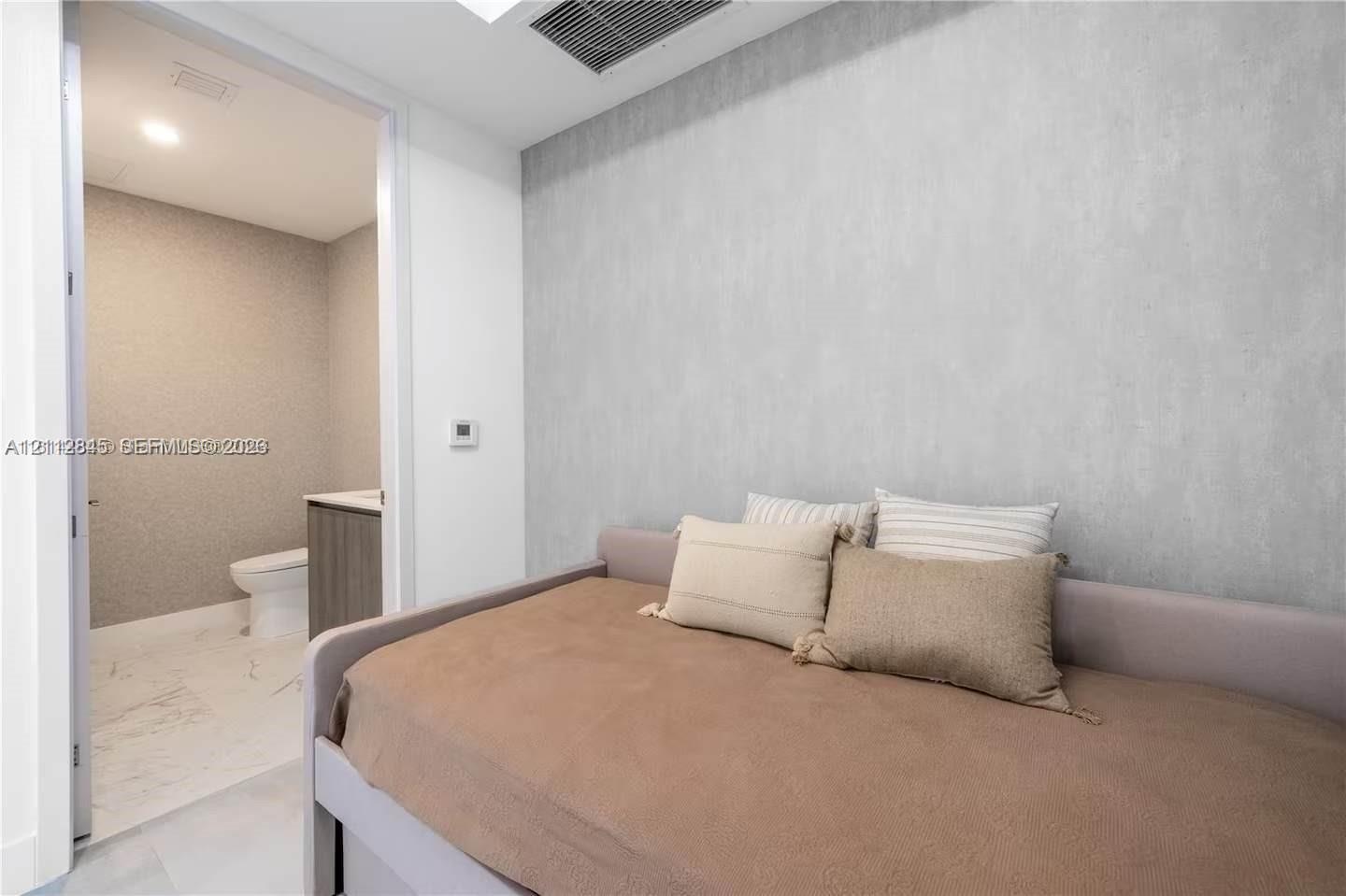 Textured accent wall, neutral interior palette, and recessed ceiling lighting, with an entry to a bathroom featuring stone-finish floor tiling and a f