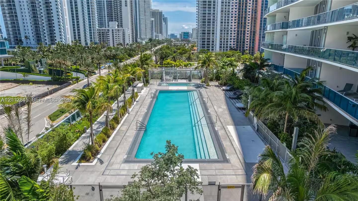Rectangular swimming pool featuring integrated entry steps and stone paver decking surrounded by mature palm trees and glass-railed balconies
