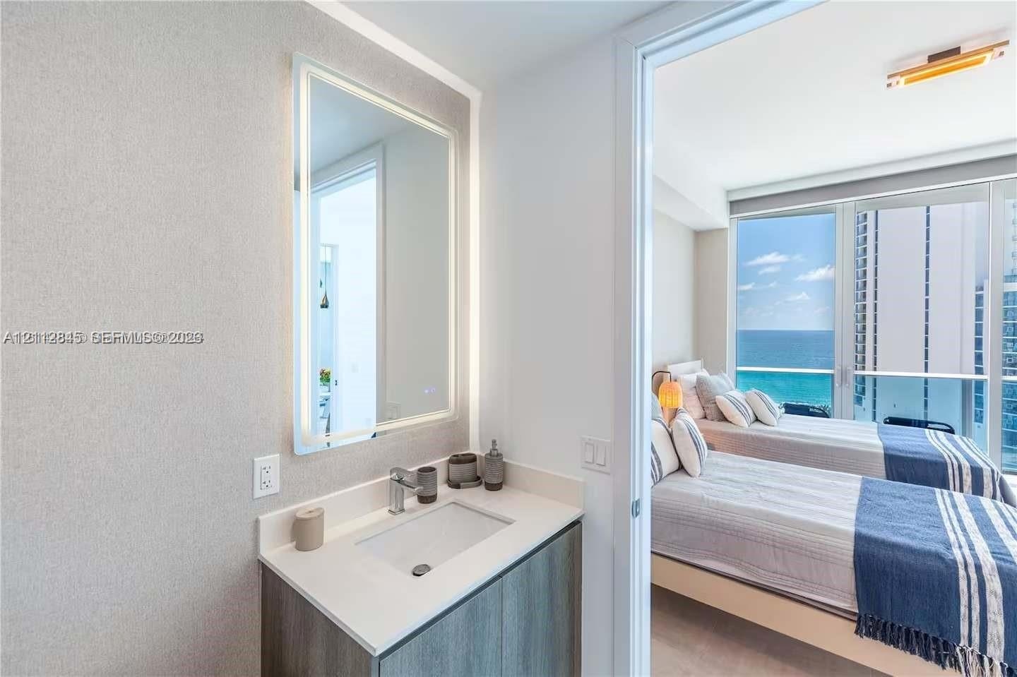 Vanity featuring a stone-composite countertop, undermount sink, integrated LED-backlit mirror, and wood-finish cabinetry, paired with floor-to-ceiling