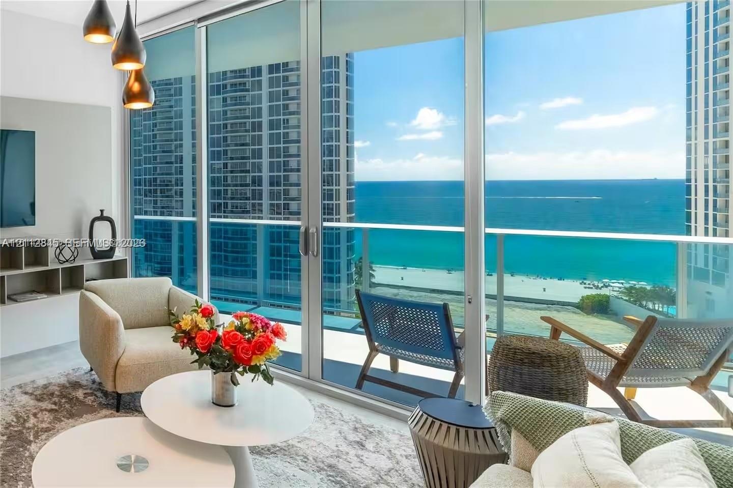 Floor-to-ceiling glass walls, expansive balcony with glass railings, built-in media shelving, and trio of pendant light fixtures