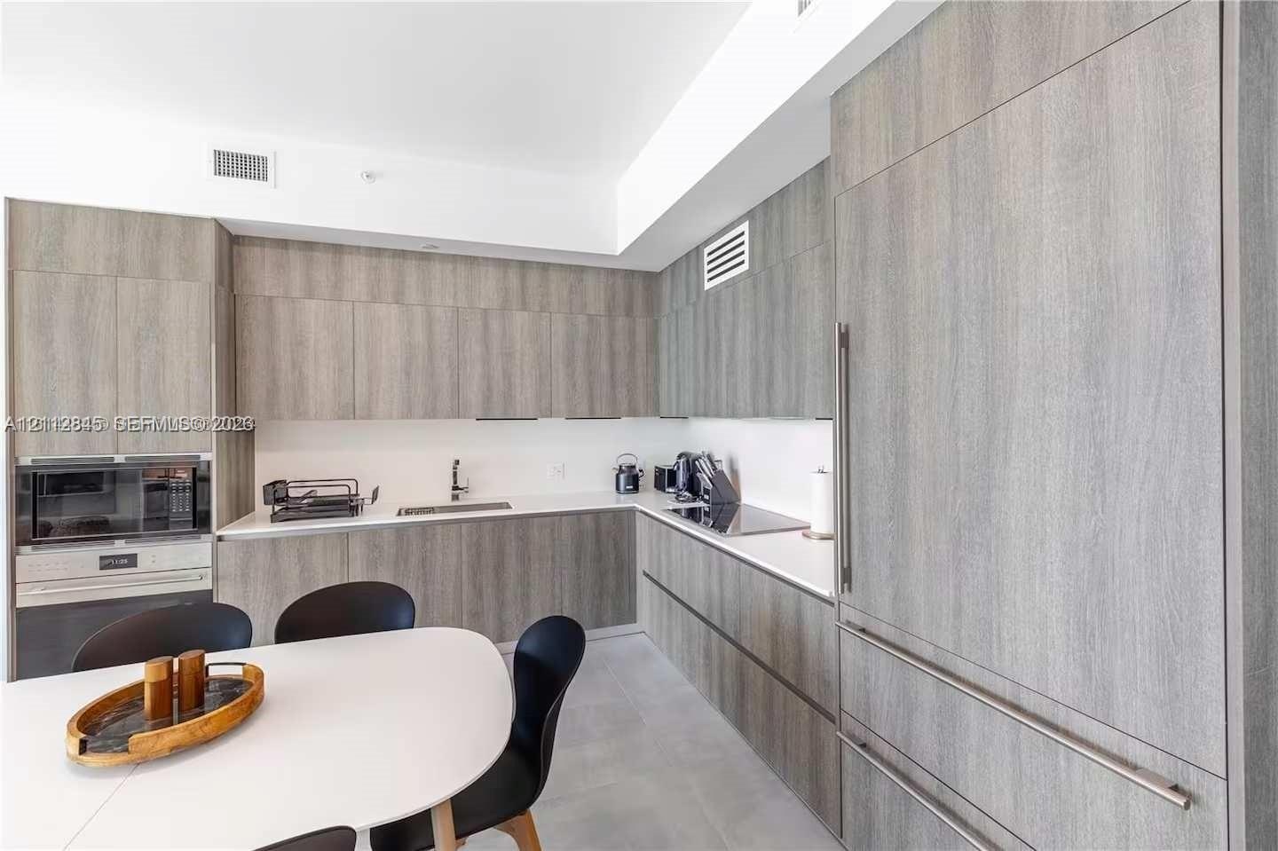 Kitchen featuring flat-panel wood-finish cabinetry, integrated panel-ready refrigerator, solid-surface countertops, built-in microwave, and flush-moun