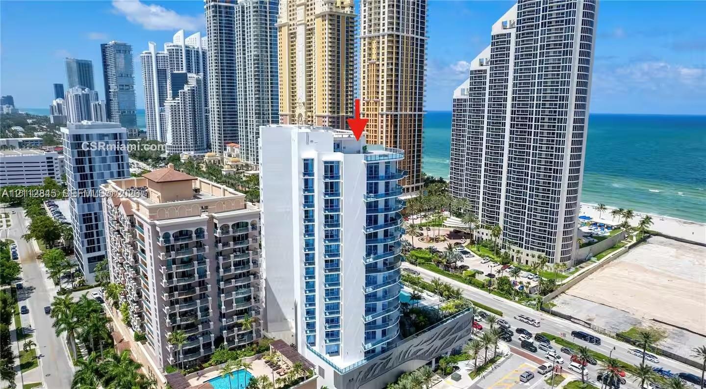 High-rise residential tower featuring blue glass-panel balconies, concrete facade, and proximity to the coastline