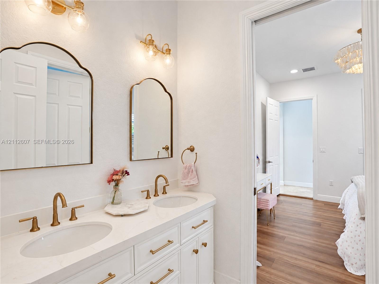 Dual-sink vanity with a white solid-surface countertop, brass-toned fixtures, arched wall-mounted mirrors, and coordinated wall sconces