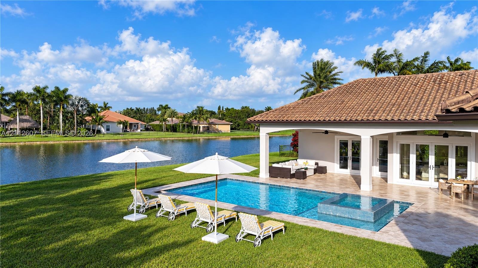 Rear exterior featuring a covered patio, a rectangular swimming pool with an integrated spa, stone-tile decking, and a waterfront location