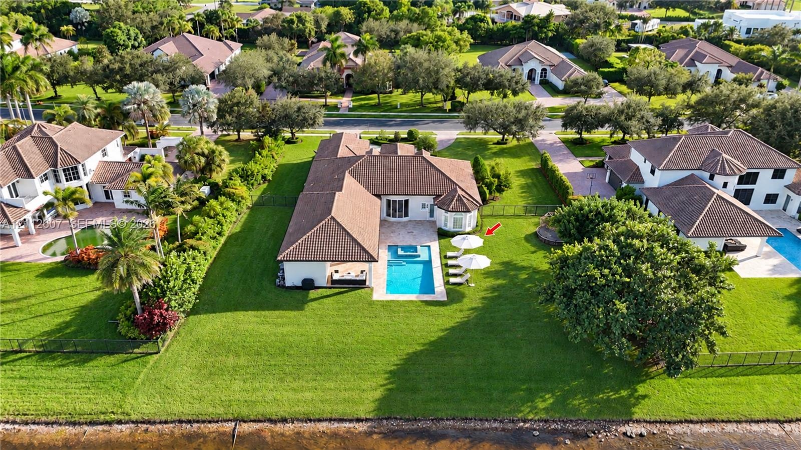 Expansive waterfront lot featuring a rectangular swimming pool, integrated spa, covered patio, and manicured lawn