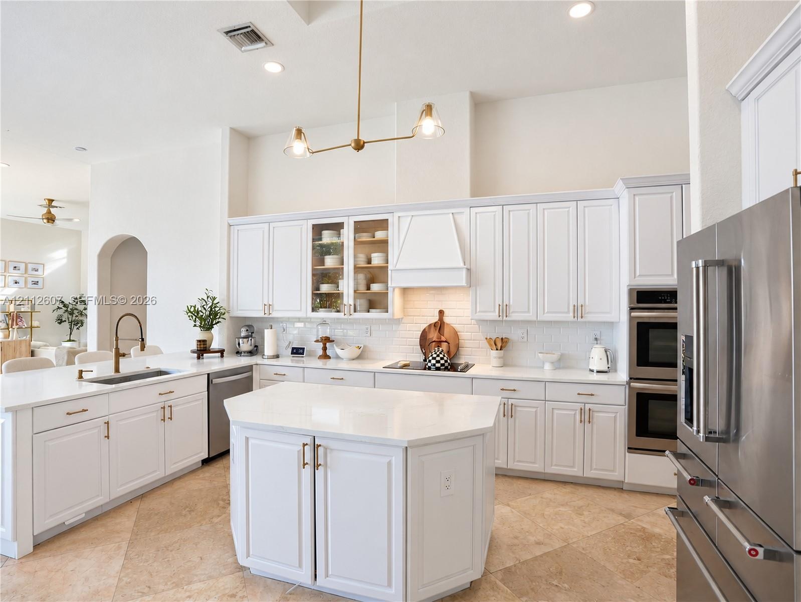 Kitchen featuring white shaker-style cabinetry, central island with stone-finish countertops, stainless steel double wall ovens, brick-pattern backspl